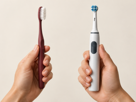 Two hands holding an electric toothbrush and a manual toothbrush for comparison